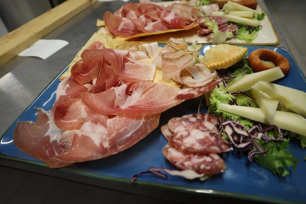Antipasto di Zinnibiri: prosciutto, pancetta, salame, formaggio e carasau su piatto blu con insalata e cavolo viola